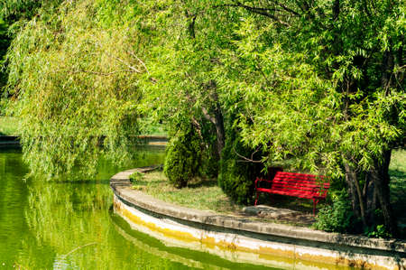 Red bench near an emerald green lake and trees.の写真素材