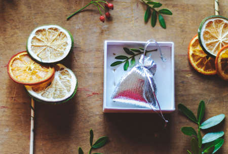 Silver gift bag in a box on wooden table surrounded by decorative dehydrated lemons and oranges on canesの写真素材
