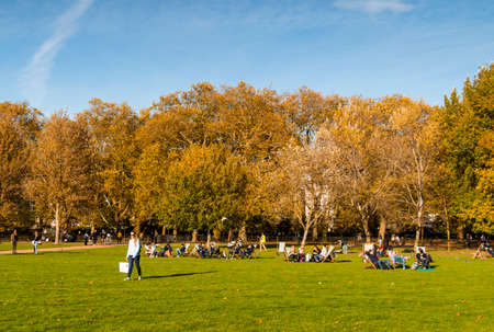 People enjoying a sunny autumn day in London, sitting on the grass in Hyde park.のeditorial素材