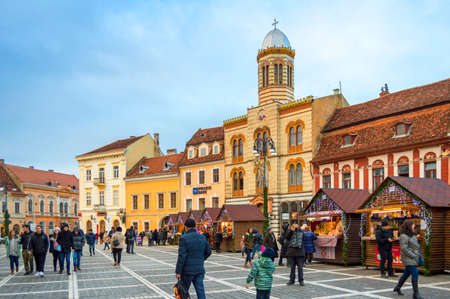 People visiting the Christmas market in Brasov. The Orthodox Church of the Birth of the Mother of God in the background.のeditorial素材