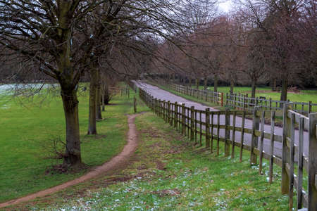 Alley and wooden fence in Cranford Park on an overcast day after a mild snowfall in March.