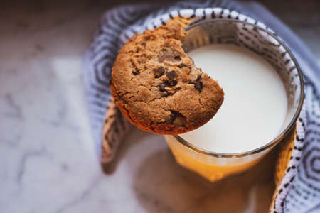 Top view of hot milk in a glass wrapped in cloth and placed on white marble table, with a chocolate chip cookie on top. Representation of self-care idea.の写真素材