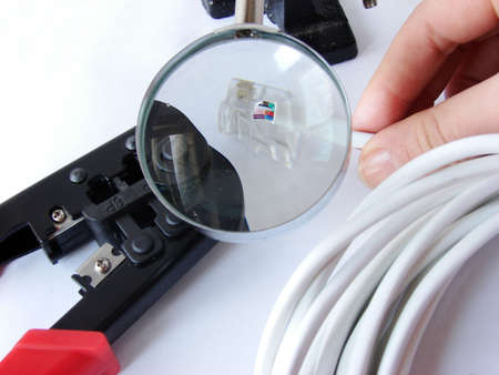 Hands cheking the network cable (cat5e) under a magnifier& crimper is under it.                               の写真素材