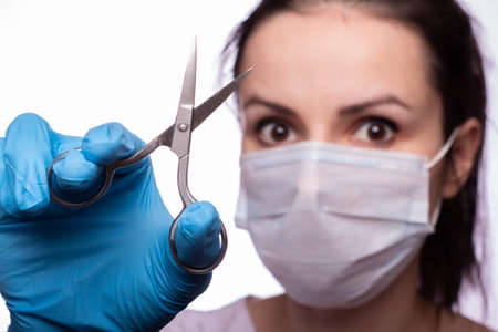 young woman in medical mask on her face, gloves on hands, scissors
