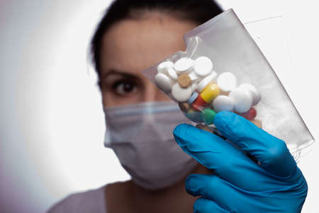 young woman in a medical poppy and gloves with a bag of pillsの写真素材