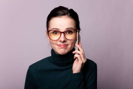 girl in a green turtleneck and glasses for sight communicates on the phone, portrait on a gray...