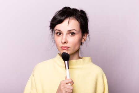 woman in a yellow sweater does makeup with a brush