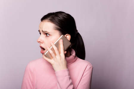 girl in a pink sweater speaks on the phone, gray background