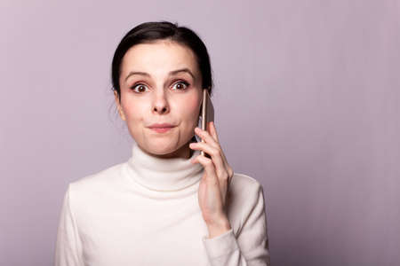 girl in a white turtleneck talking on the phone, portrait on a gray background