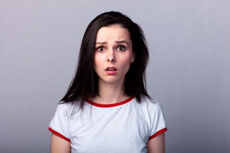 brunette woman in a T-shirt, facial emotions, pure white skin, gray background
