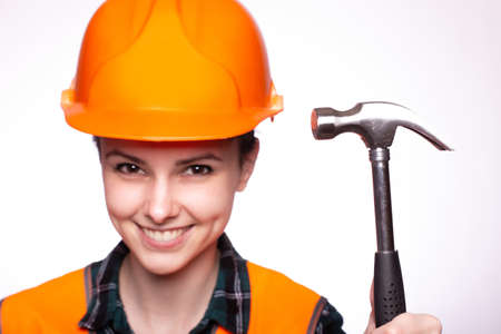 attractive woman builder in a protective helmet and an orange vest with a hammer in his hands, a hardware storeの写真素材