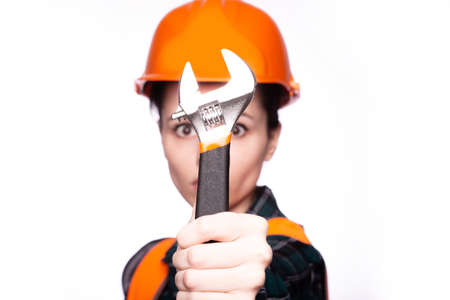 beautiful young woman worker in a helmet holds in her hand a wrenchの写真素材