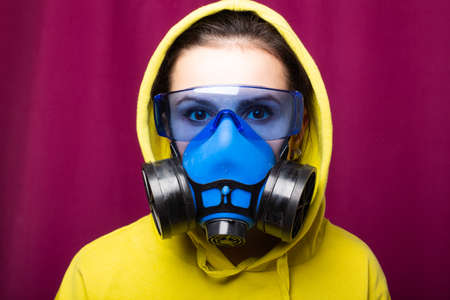 beautiful woman in blue respirator mask, goggles and green hoodie, pink studio backgroundの写真素材
