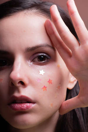 beautiful woman with shiny stars on her face, close-up portrait on a red background
