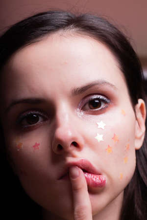 beautiful woman with shiny stars on her face, close-up portrait on a red backgroundの写真素材