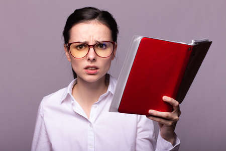 girl in a white shirt and glasses holds a red notebook in her hand