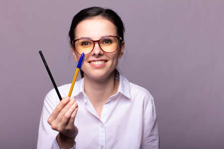 girl in a white shirt and glasses holds a pencil and a pen in her handの写真素材
