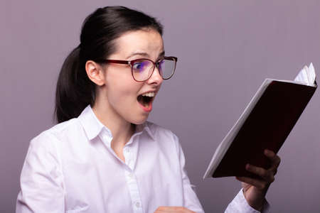 woman manager in a white shirt and glasses holds a red notebook in her handの写真素材