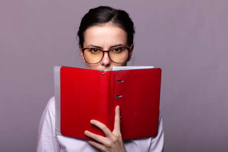 woman manager in a white shirt and glasses holds a red notebook in her hand