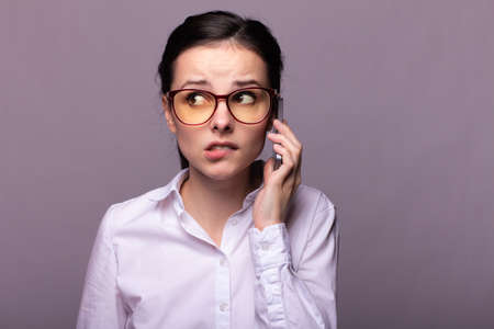 woman in white shirt and glasses talks on the phone and gets upsetの写真素材
