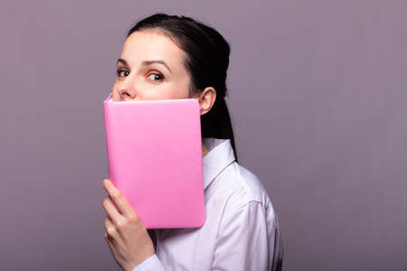 girl in a white shirt holds a pink notebookの写真素材