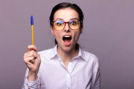 girl office manager in glasses and a white shirt holds a pen, gray background, idea
