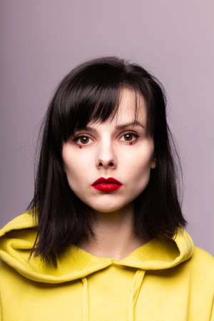 woman in a hoodie with red lipstick on the lips and dots under the eyes
