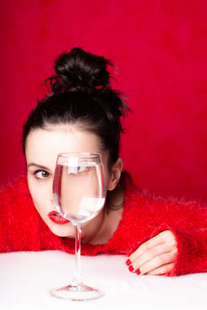 beautiful girl in red looks through a glass of water, art portrait, red color prevailsの写真素材