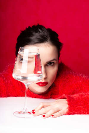 woman in red looks through a glass of water, art portraitの写真素材
