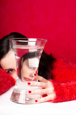 beautiful girl with red lipstick on her lips in a red sweater with a glass of water, red backgroundの写真素材