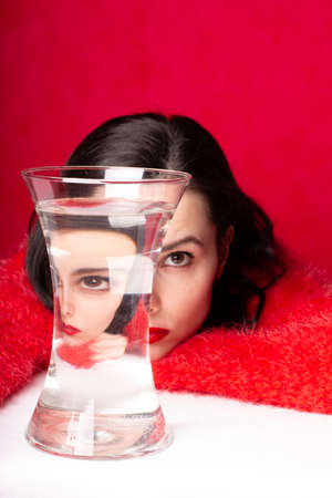 beautiful girl with red lipstick on her lips in a red sweater with a glass of water, red backgroundの写真素材