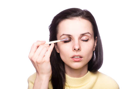 woman makeup artist in a yellow sweater draws eyebrows, light backgroundの写真素材