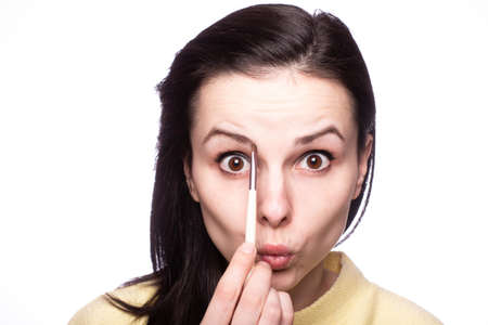 woman makeup artist in a yellow sweater draws eyebrows, light background
