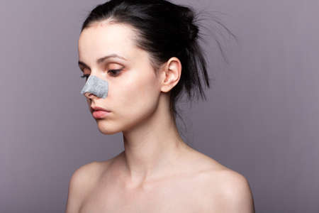woman with bare shoulders and a plaster on her nose against black dots, problem skin, gray backgroundの写真素材