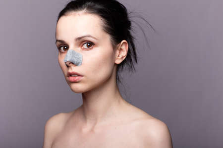 woman with bare shoulders and a plaster on her nose against skin pollution, problem skin, gray backgroundの写真素材