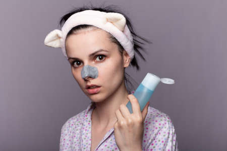 woman holds in her hands a cosmetic bottle with a face tonic, a plaster from blackheads on the nose,...