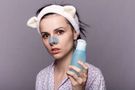 woman holds in her hands a cosmetic bottle with a face tonic, a plaster from blackheads on the nose,...