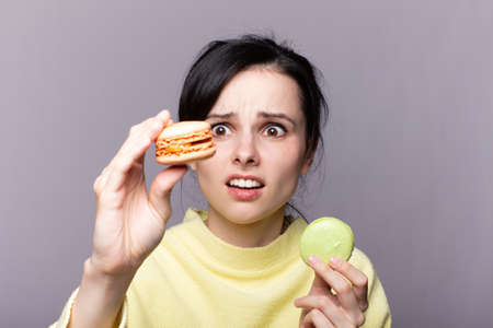 Young brunette woman over isolated studio  holding colorful French macaronsの写真素材