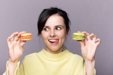 Young brunette woman over isolated studio   holding colorful French macarons