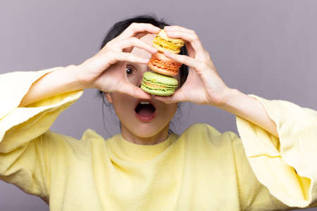 Young brunette woman over isolated studio  holding colorful French macarons