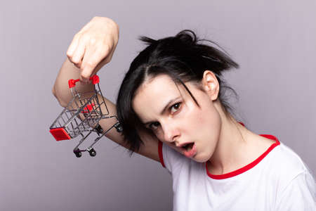 Woman showing mini shopping cart on grey