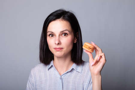 cute girl in an gray shirt holds macaroon cookies in her hands, gray backgroundの写真素材