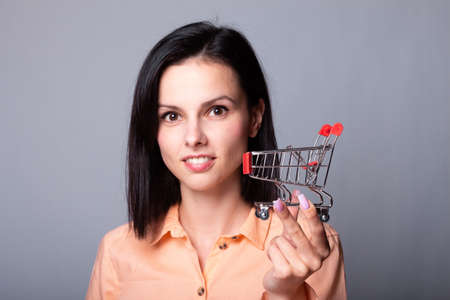 woman in an orange shirt holds a small shopping cart in her handsの写真素材