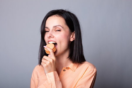 Young brunette woman over isolated gray background holding colorful French macarons