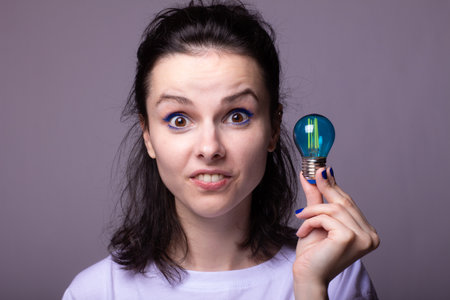 beautiful girl in a white t-shirt holds a blue light bulb in her handsの写真素材