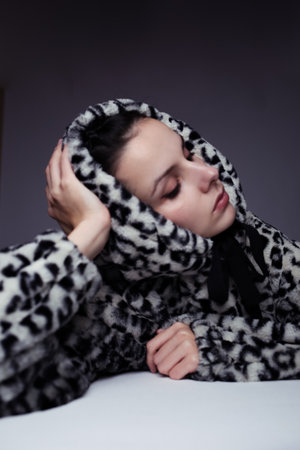 a woman in a leopard print hoodie lay down on a table with a white tablecloth, gray background, art...