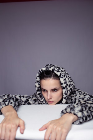 a woman in a leopard print hoodie lay down on a table with a white tablecloth, gray background, art portraitの写真素材
