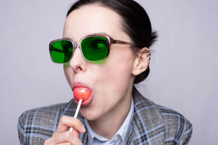woman in an office suit in a cage and green glasses eating a lollipopの写真素材