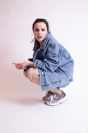 woman in denim jacket, shorts and sneakers, on white studio background