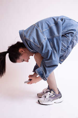 woman in denim jacket, shorts and sneakers, on white studio background